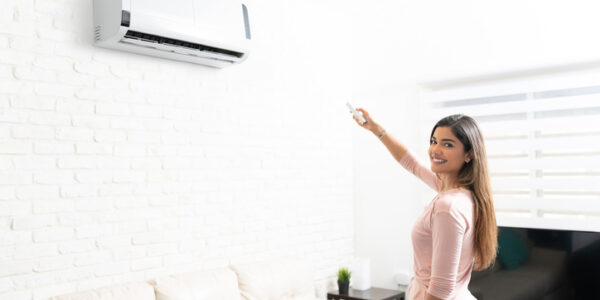 Hispanic pretty woman turning on air conditioner using remote control in living room at home